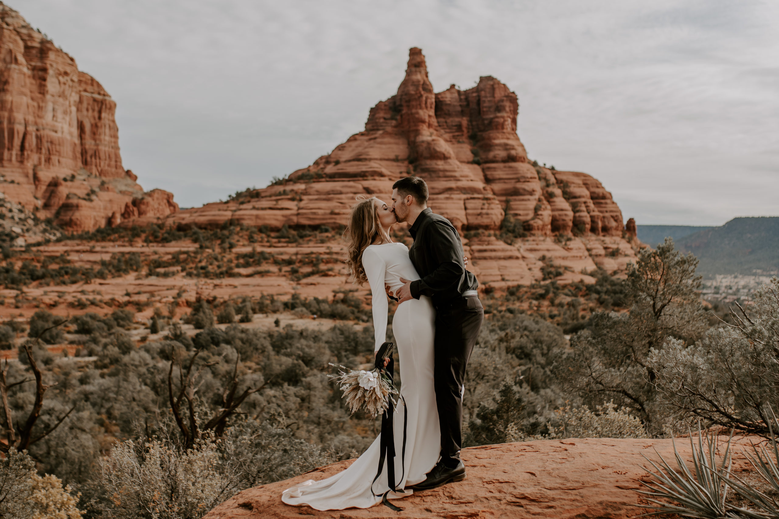 Bride and groom share a kiss with the grand view of the red rocks in Sedona, Arizona during their adventurous elopement, taken by Off Path Photography