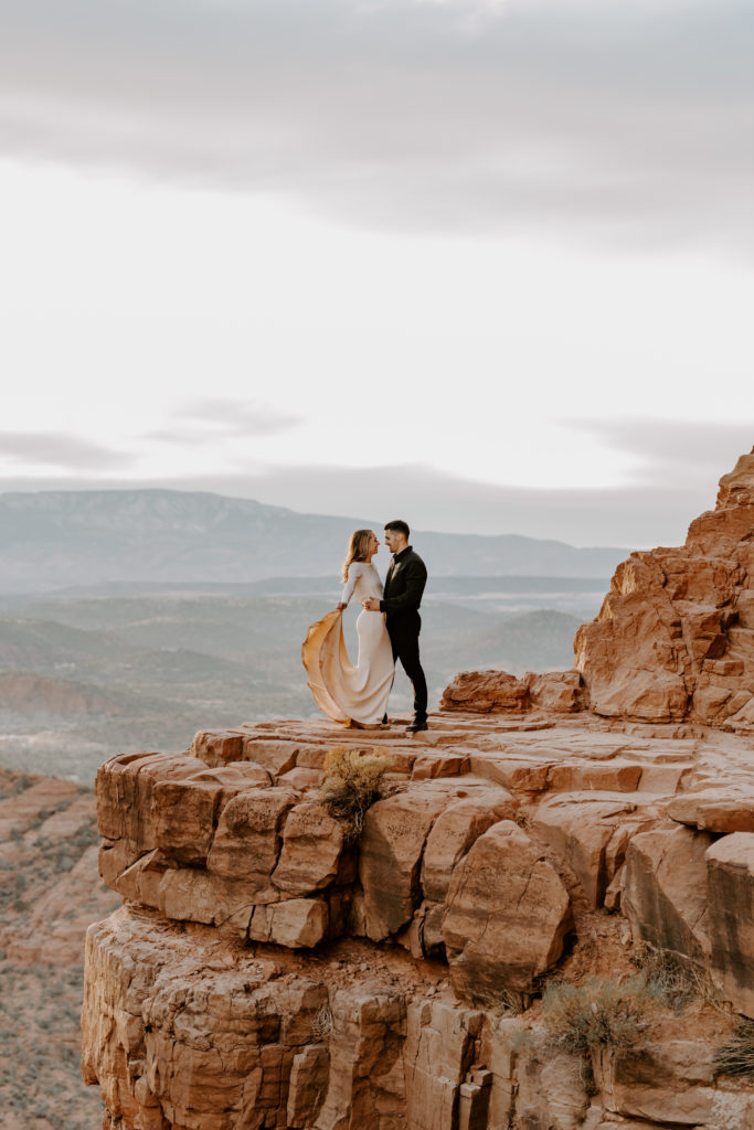 A bride and groom pose on the edge of a cliff