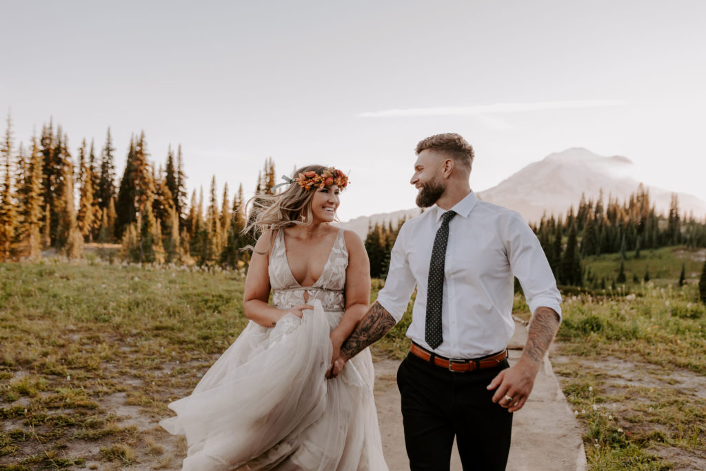 Bride and groom hold hands while smiling at each other during their adventure elopement in the forest captured by Off Path Photography