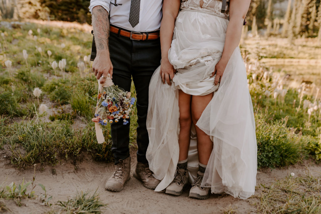 A close up shot of bride lifting up her dress to expose her hiking boots as she stands near her groom before their adventurous mountain elopement