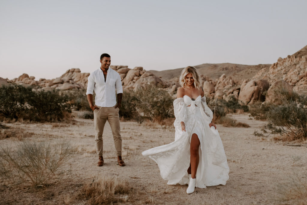 Groom looks at bride as she strolls through Joshua Tree National Park for their elopement shoot, captured by Off Path Photography