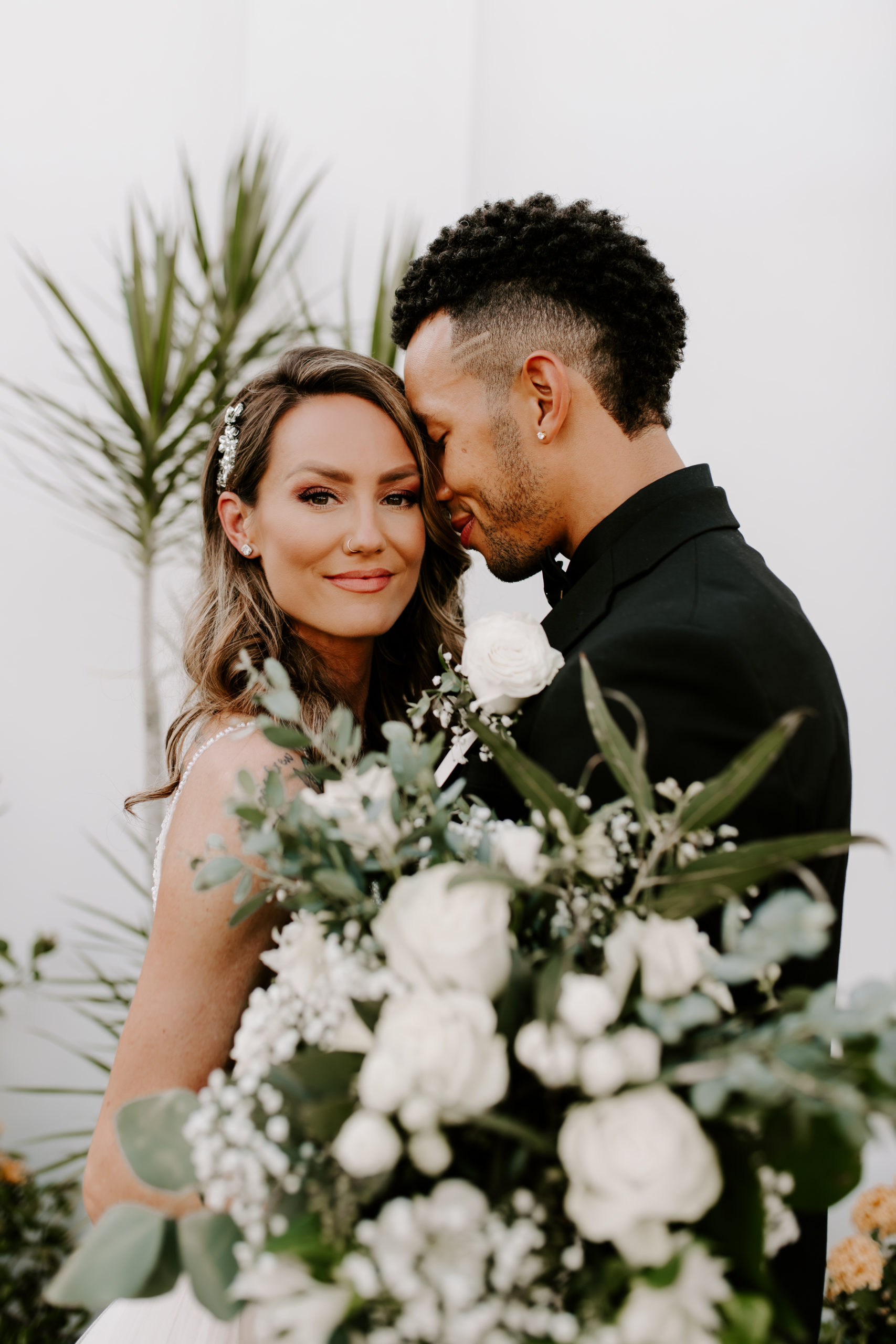 Groom presses his head against the bride's as she smiles enchantingly at the camera while holding her bridal bouquet, captured by Off Path Photography