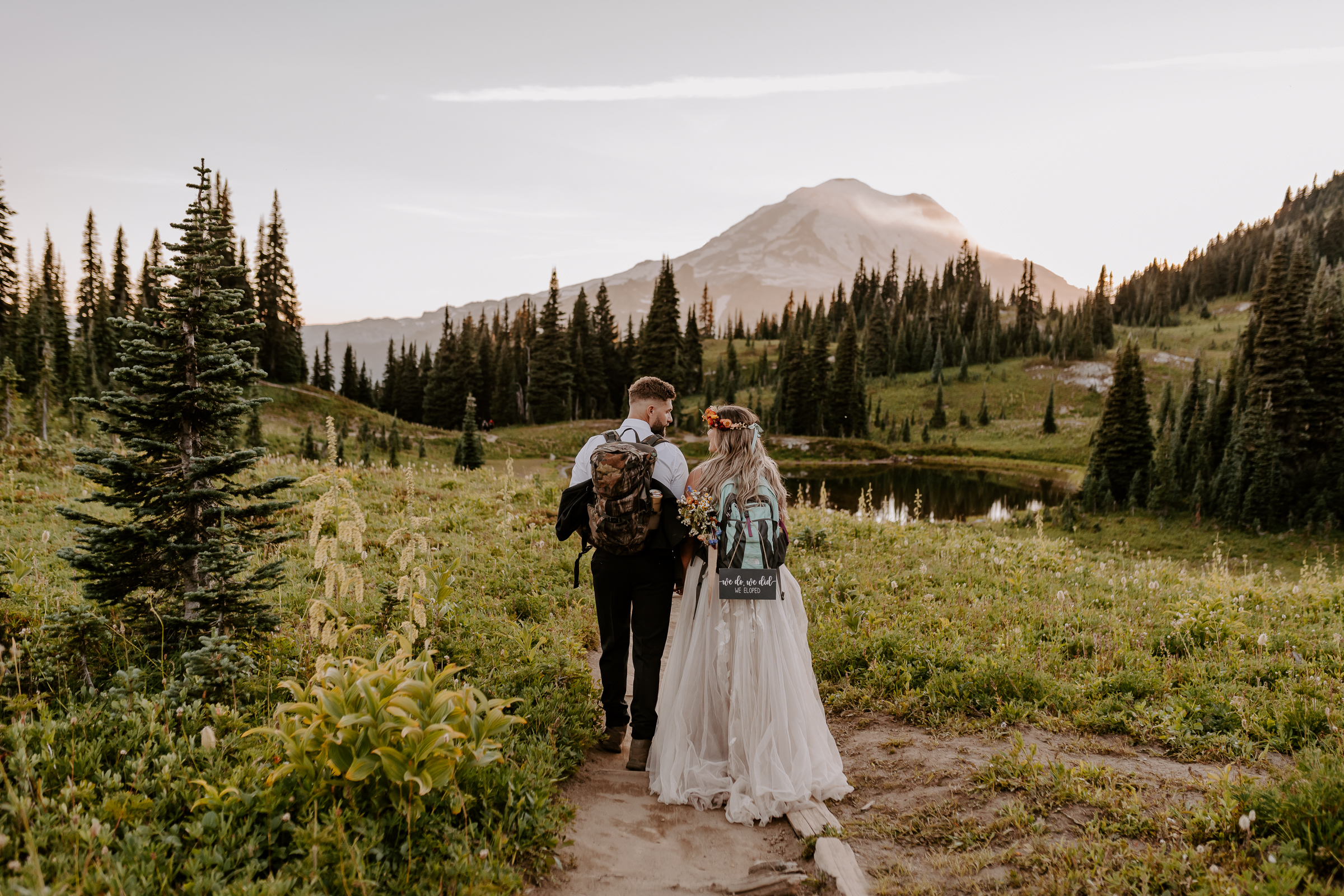 Couple, with their backs to the camera, strolling through Mt. Rainier National Park with their hiking backpacks on, captured by Off Path Photography