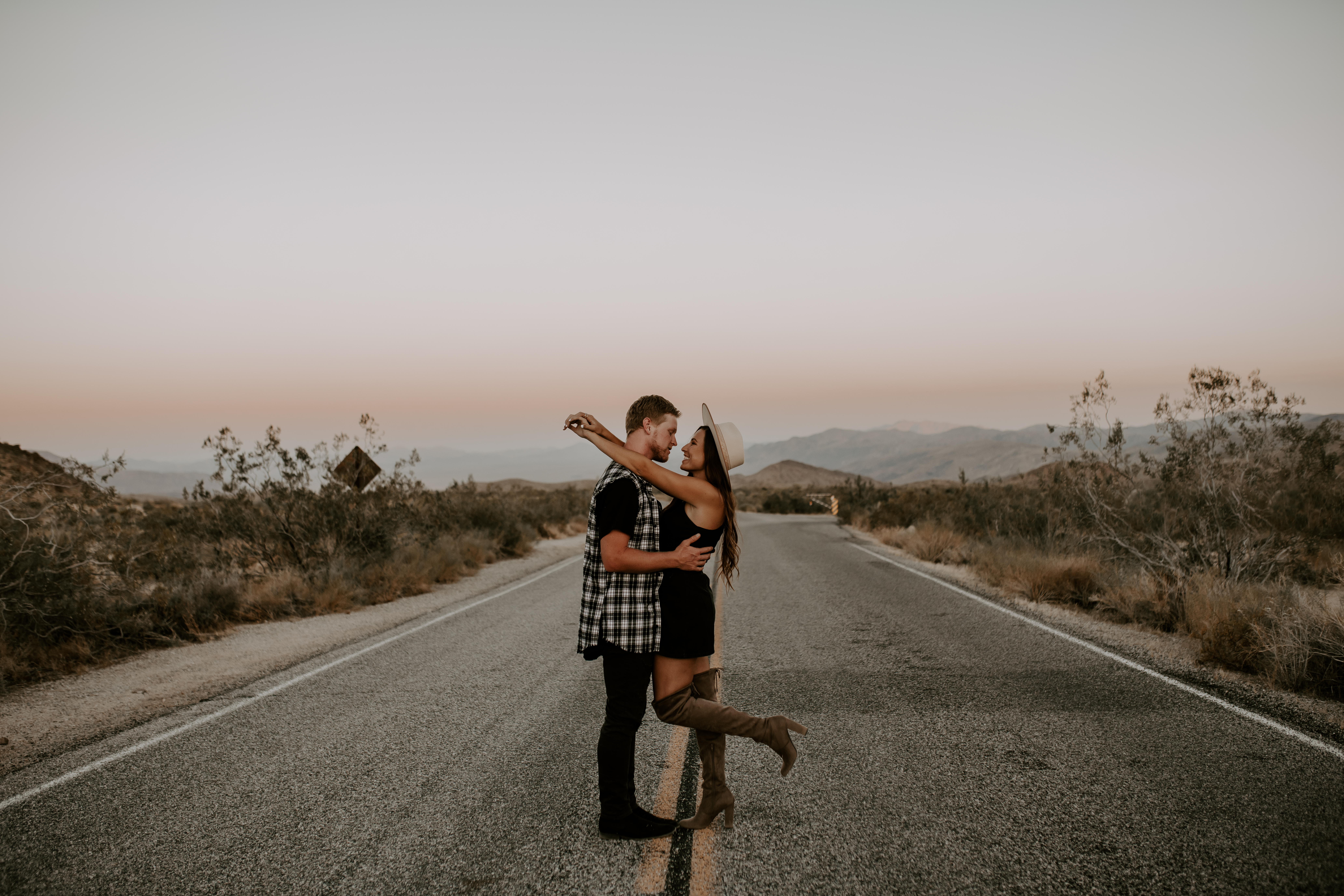 Couple wrap their arms around each other in the middle of the highway during their Romantic and Carefree Joshua Tree Photoshoot