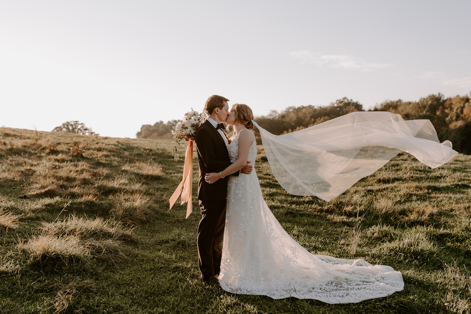 Couple sharing a kiss in the middle of a field in Sonoma County with the wind blowing brides veil